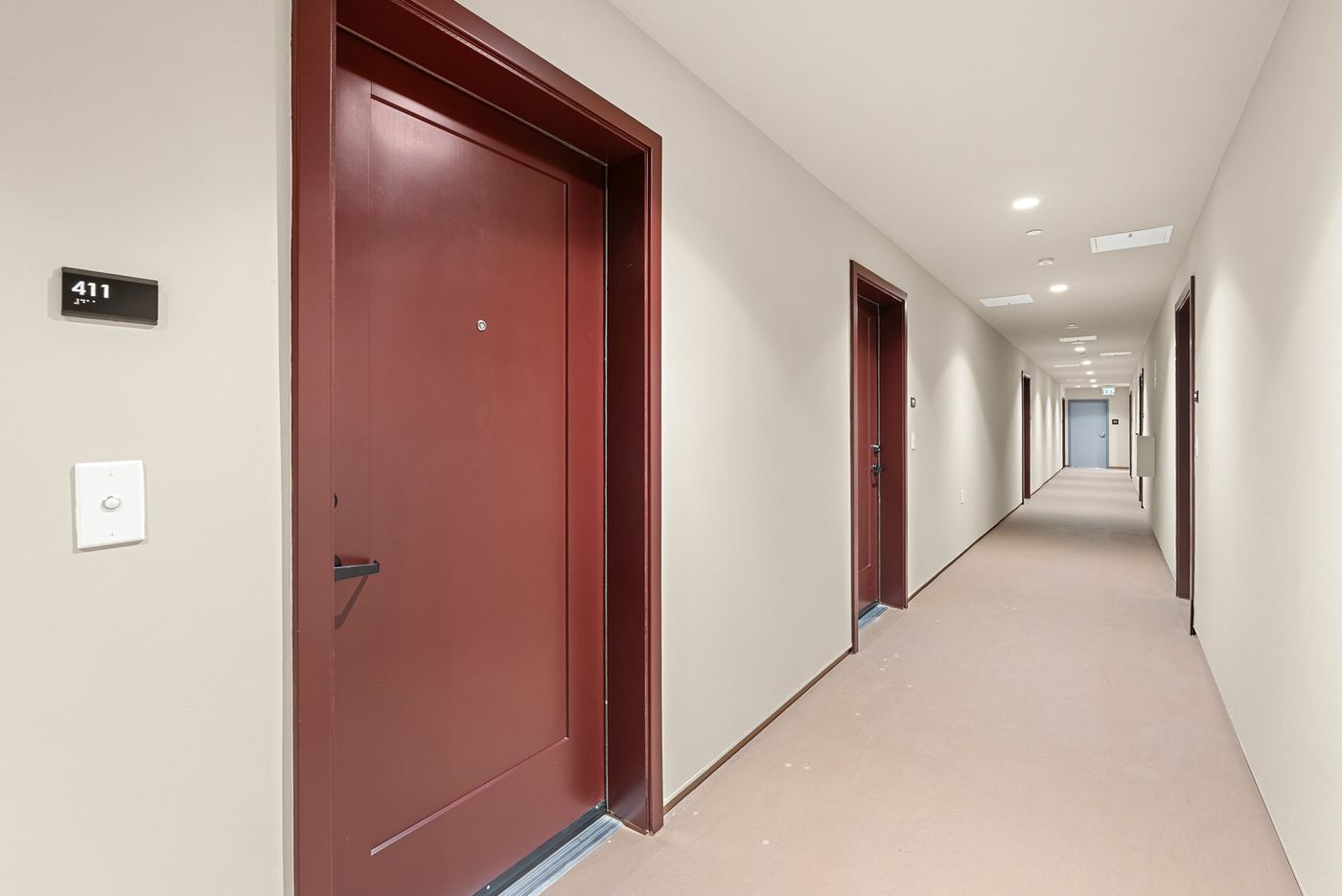 An interior hallway on an upper floor, with apartment doors, unit numbers and a light-colored floor.