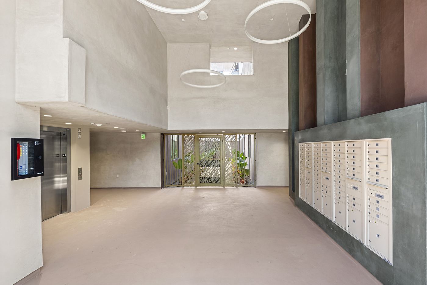 The entry lobby. An open double-height space with the mailboxes on one wall, an elevator, and glass doors to the courtyard.
